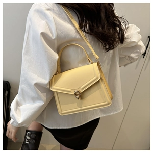 Detail of creamy yellow leather handbag showing golden twist lock and textured finish
