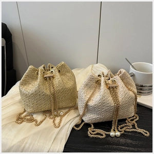 Detail of straw woven bucket bag with gold chain strap and elegant pearl accents