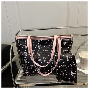 Detail of black tote bag set featuring pink bow and heart patterns on metal display