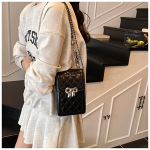 Detail of black quilted phone bag featuring a silver metal bow and woven chain strap
