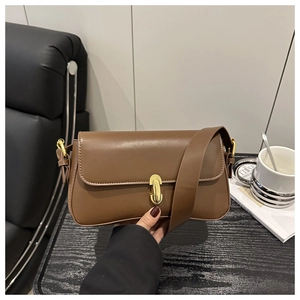 Close-up of brown leather shoulder bag featuring a gold metal buckle and wide strap