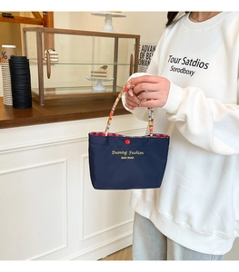 Close-up of small navy blue handbag with colorful woven handle and yellow logo