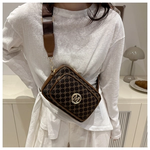 Detail of a brown monogram camera bag with a metal M logo and wide fabric strap