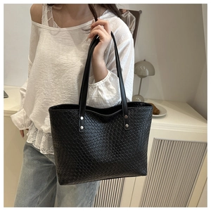 Detailed close-up of a black woven tote bag with silver rivets and textured checkerboard pattern