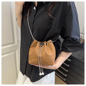 Detail of caramel bucket bag featuring crocodile pattern, butterfly buckle and pearl accent