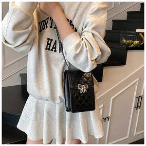 Detail of black quilted leather phone bag with silver bow buckle and elegant chain strap