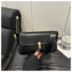 Detail of minimalist black underarm bag with elegant gold metal lock and smooth texture
