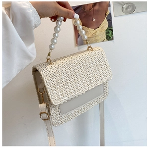 Close-up of cream woven straw crossbody bag featuring a large pearl handle and gold hardware