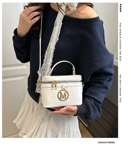 Detailed close-up of white leather mini box bag featuring a golden M-logo buckle and gold chain
