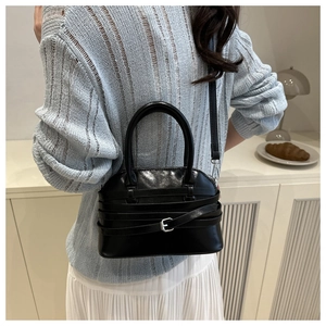 Detail of a black glossy shell bag with triple decorative straps and silver buckles