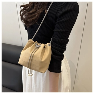 Detail of beige bucket bag featuring butterfly clasp, chain strap and pearl charms