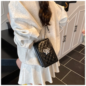 Close-up of black quilted leather crossbody bag with silver bow accent on model