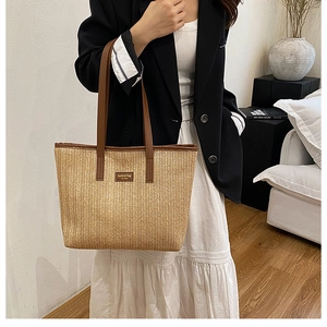 Detail of a large straw tote bag with brown leather handles and brand nameplate