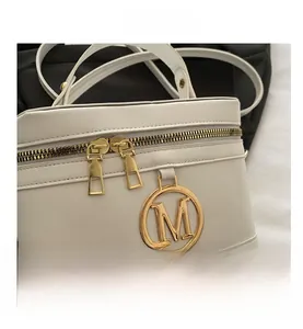 Macro shot of the white leather bucket bag featuring a gold M-shaped metal emblem