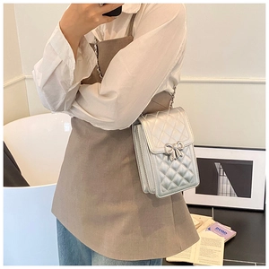 Detailed view of silver quilted crossbody bag with metal bow clasp and chain strap