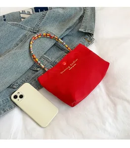 Detail of red canvas tote bag with colorful beaded handle and golden branding logo