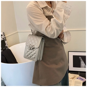 Detail of silver quilted crossbody bag featuring a delicate metal bow and chain strap