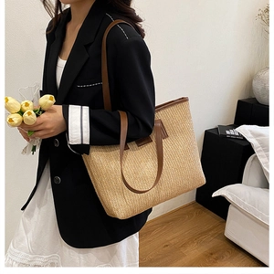 Detail of a large woven straw tote bag with brown leather straps on a model