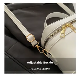 Close-up of white leather handbag featuring adjustable light gold buckle and dual zipper detail