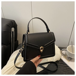 Detail of black leather handbag featuring a round gold knot buckle and stitching