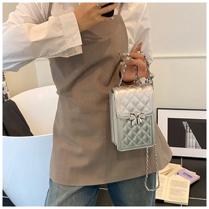 Detail of silver quilted crossbody bag with metal bow and elegant chain strap on a model