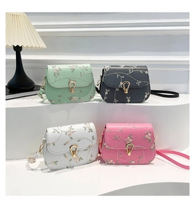 Detailed view of floral embroidery and gold horseshoe buckles on pastel crossbody bags