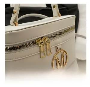 Detail of smooth gold double zippers and metallic M logo on white box handbag