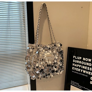 Close-up of silver sequin tote bag with woven shoulder straps on a minimalist wall
