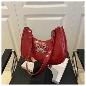 Détail du sac croissant en cuir verni rouge avec un ornement papillon en métal argenté