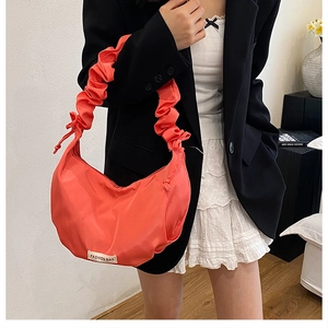 Detail of coral pleated crescent bag with fashion label on white lace dress