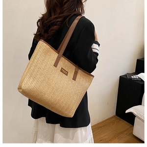 Close-up of a large woven straw tote bag with brown leather straps worn by a model
