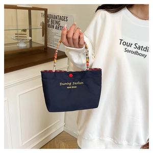 Detail of blue nylon mini tote bag with colorful braided handles and red snap button