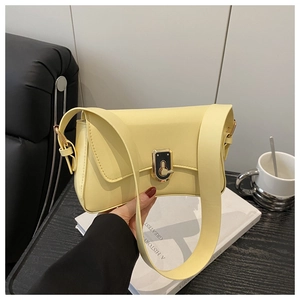 Close-up of a pale yellow minimalist shoulder bag featuring a wide strap and gold metal clasp