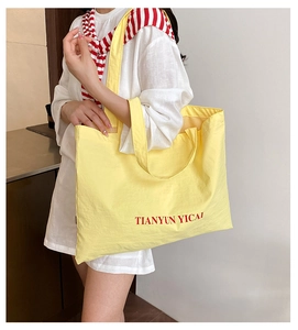 Shoulder shot of large yellow canvas tote bag with red letter print on white outfit