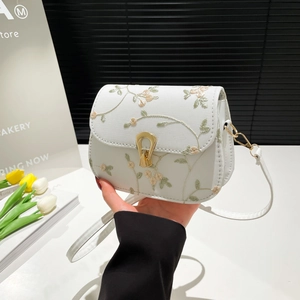 Elegant white saddle bag with floral embroidery and gold horseshoe clasp held by hand
