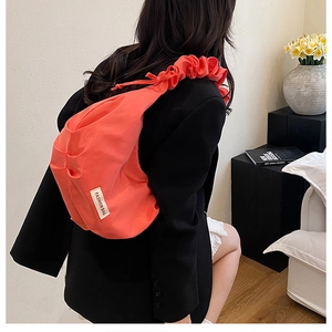 Detail view of coral nylon pleated shoulder bag with knotted strap and fashion tag