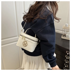 Detailed view of white box-style crossbody bag with gold M-logo worn by a model