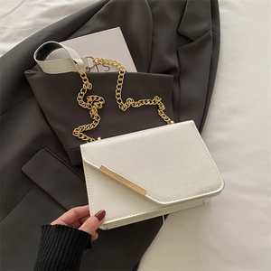 Elegant white leather crossbody bag with gold chain detail on a minimalist blazer