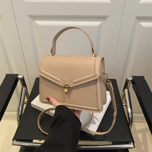 Minimalist beige structured handbag with gold twist lock and adjustable shoulder strap