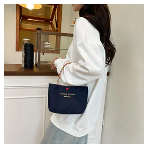 Detail of navy handbag with colorful woven handle and red button on a cafe background