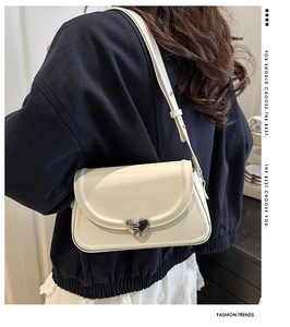 Detail of a creamy white underarm bag with a silver heart-shaped metal buckle on the flap