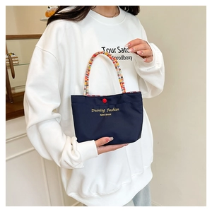 Macro shot of embroidered navy tote bag with colorful braided handles and red button