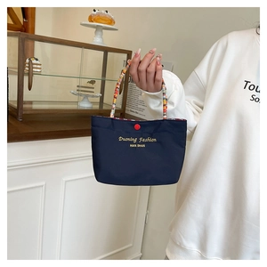Detail of navy blue mini handbag with colorful woven rope handle and snap button close