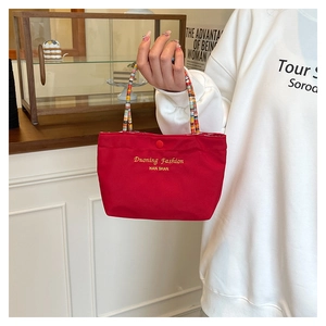 Detailed view of red fabric handbag with colorful woven handle and gold branding