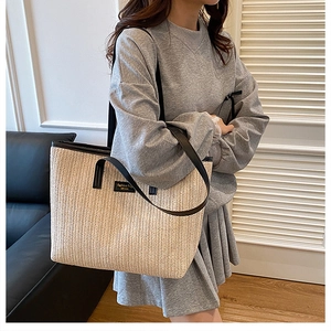 Detail of woven straw tote bag with black handles and fashion tag on the beige surface