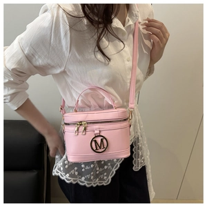 Détail du sac seau rose avec logo M doré, porté avec une chemise blanche en dentelle