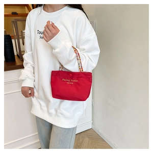 Detail of red small handbag featuring colorful braided rope handles and gold brand logo