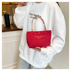 Detail of red canvas handbag with colorful braided handle and gold lettering logo