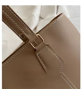 Detail of a brown leather tote bag handle with golden hardware and white contrast stitching