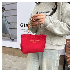 Detail of red canvas tote with gold embroidery and colorful woven handle closure
